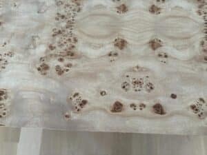 Close-up of a light-colored wood surface with distinctive, symmetrical knotted and swirled grain patterns.