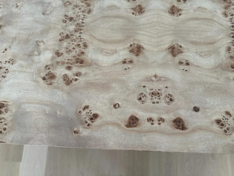 Close-up of a light-colored wood surface with distinctive, symmetrical knotted and swirled grain patterns.