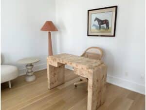 Minimalist office with a light wood desk, wicker chair, floor lamp, side table, and horse painting on the wall.