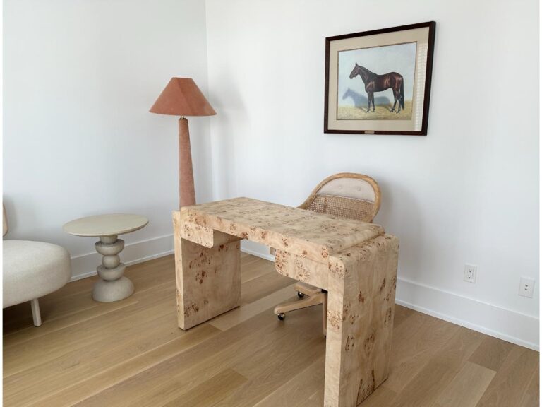 Minimalist office with a light wood desk, wicker chair, floor lamp, side table, and horse painting on the wall.