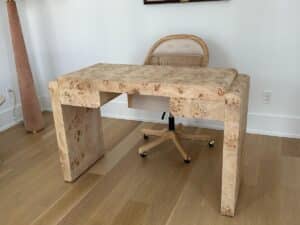 A light wood desk with matching chair on casters in a minimalist room with light wood flooring.