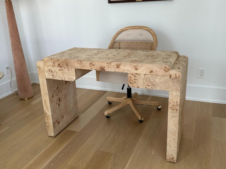 A light wood desk with matching chair on casters in a minimalist room with light wood flooring.