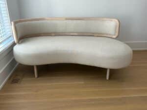 Curved, modern beige sofa with light wood frame on light wood floor near a window.