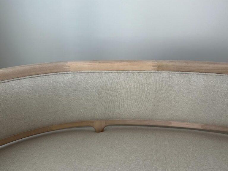 Curved light wood and beige fabric sofa against a plain, light gray wall.