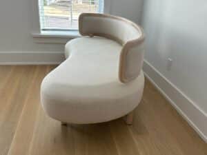 Curved, cream-colored loveseat with wooden trim, placed in a bright room with wood floors.