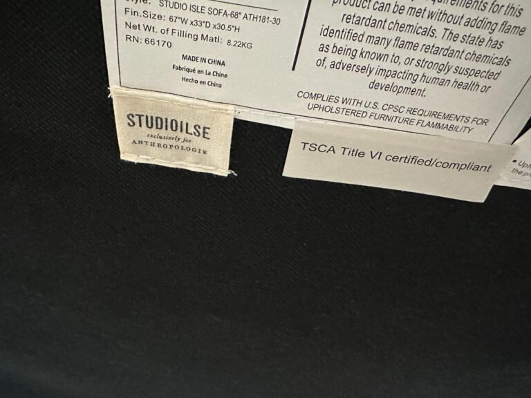 Fabric and safety labels on a piece of furniture, including StudioIlse and TSCA Title VI compliance tags.