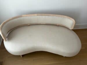 Curved, cream-colored sofa with wooden frame on a light wood floor against a white wall.