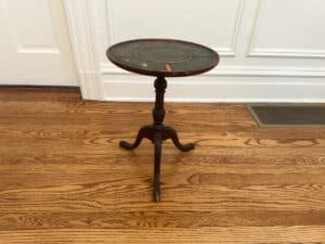 An Antique Side Table on a hardwood floor in front of a white paneled wall.