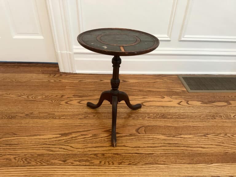 An Antique Side Table on a hardwood floor in front of a white paneled wall.