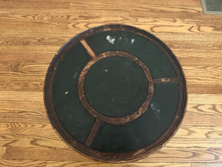 An Antique Side Table with a round, weathered wooden surface and a green center sits atop a hardwood floor.
