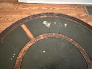 Underside of an "Antique Side Table" with worn green paint and visible wooden supports, set on a wooden floor.