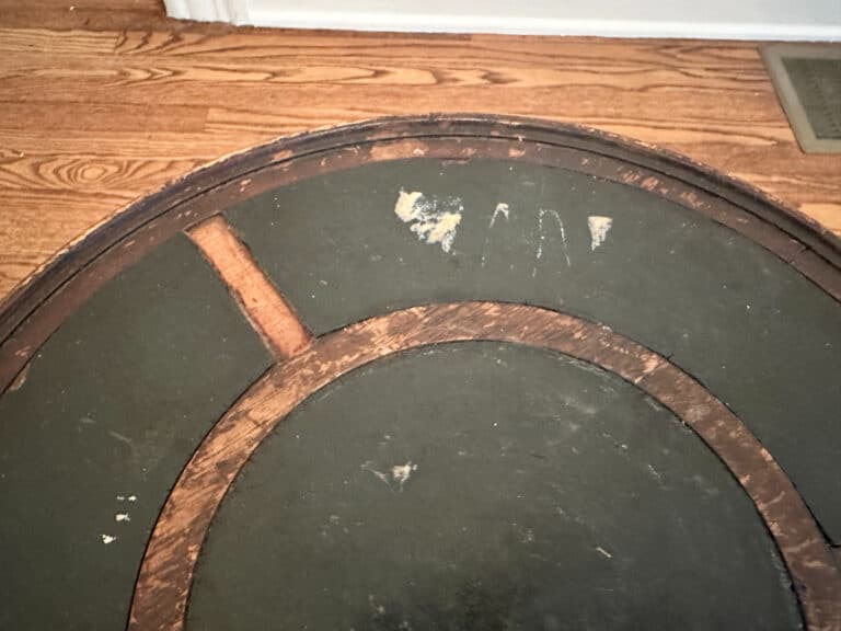 Underside of an "Antique Side Table" with worn green paint and visible wooden supports, set on a wooden floor.