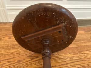 Antique Side Table's wooden pedestal base on a hardwood floor, displaying wear and scratches.