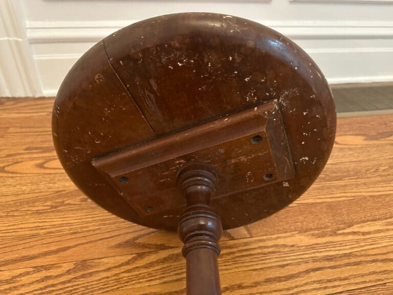 Antique Side Table's wooden pedestal base on a hardwood floor, displaying wear and scratches.