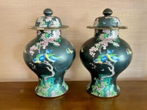 Two ornate, black porcelain vases with lids, featuring blue birds and floral designs against a wooden background.