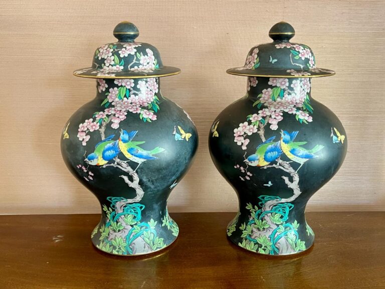 Two ornate, black porcelain vases with lids, featuring blue birds and floral designs against a wooden background.