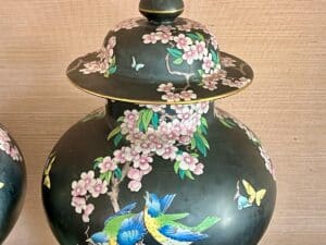 Ornate black vase with colorful birds, butterflies, and pink cherry blossoms on a textured background.
