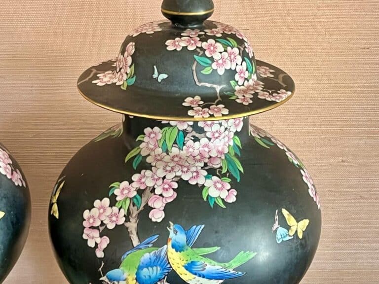 Ornate black vase with colorful birds, butterflies, and pink cherry blossoms on a textured background.