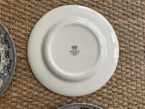 Back of a white ceramic plate with a logo, on a woven-texture surface.
