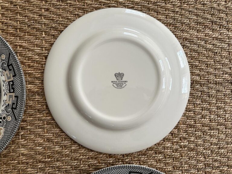 Back of a white ceramic plate with a logo, on a woven-texture surface.