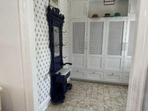 Hallway with white lattice cabinets, blue vintage coat stand, and patterned wallpaper.