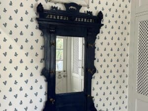 Ornate black mirror on a floral-patterned wall with a partial view of a white door.