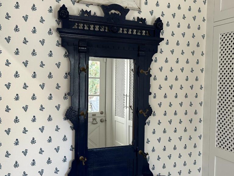 Ornate black mirror on a floral-patterned wall with a partial view of a white door.