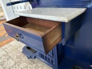 Open drawer in a blue wooden cabinet with a marble top, indoors on a tiled floor.