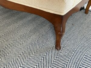 Close-up of a wooden furniture leg on a black-and-white chevron patterned carpet.