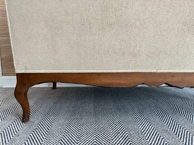 A Chenille Upholstered Settee on a chevron-patterned rug against a textured wall.