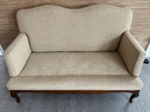 Chenille upholstered settee with a wooden frame on a herringbone-patterned carpet.