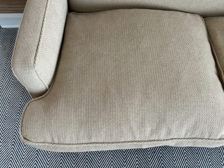 A Chenille Upholstered Settee with a beige textured cushion, placed on a herringbone-patterned rug.
