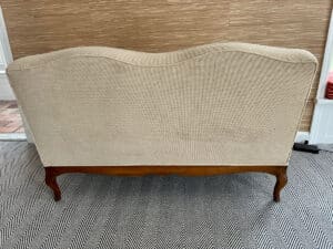 A chenille upholstered settee with wooden legs on a black and white zigzag rug.