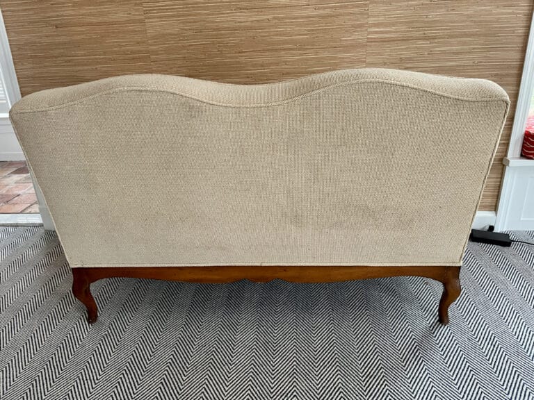 A chenille upholstered settee with wooden legs on a black and white zigzag rug.