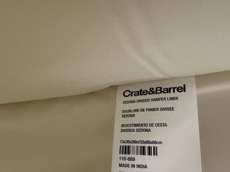 Close-up of a Crate & Barrel label on a cream-colored Sedona divided hamper liner, made in India.