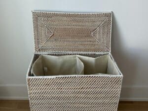 A white wicker laundry basket with an open lid and two fabric-lined compartments inside.