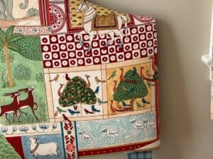 Colorful textile with animal and nature motifs, including horses, birds, and geometric patterns on a draped surface.
