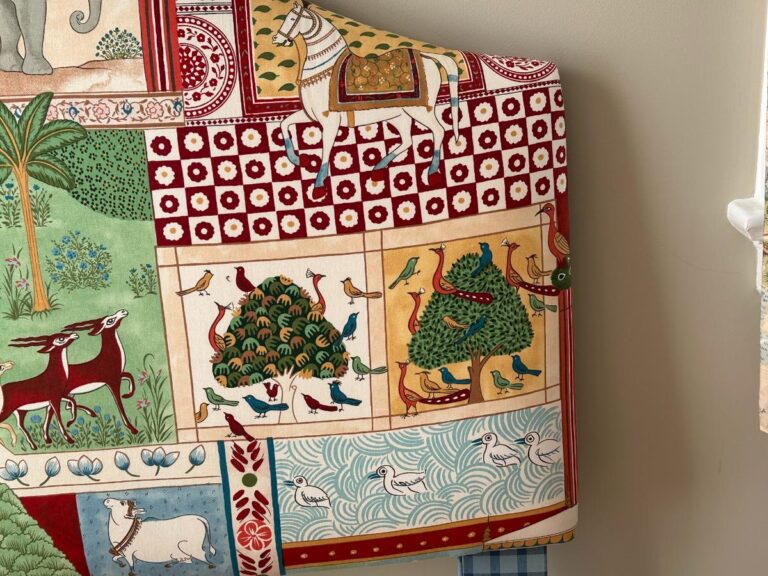 Colorful textile with animal and nature motifs, including horses, birds, and geometric patterns on a draped surface.