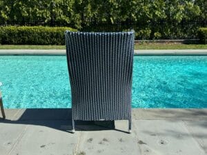 Wicker chair beside a clear blue swimming pool, surrounded by greenery.