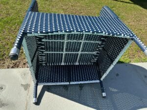 Upside-down wicker chair with blue and white pattern on a concrete surface, grass in the background.