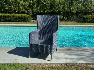 A black and white woven chair by a pool, with trees in the background on a sunny day.