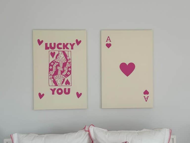 Two wall art pieces: a queen of hearts with "Lucky You" and an ace of hearts above white pillows.
