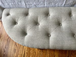 Demilune Tufted Bench on wooden floor with a quilted fabric backdrop.