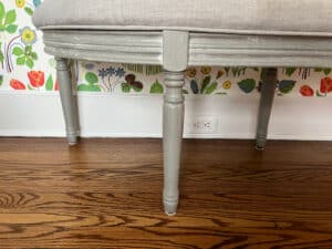 The Demilune Tufted Bench sits on a hardwood floor against a floral wallpaper backdrop.