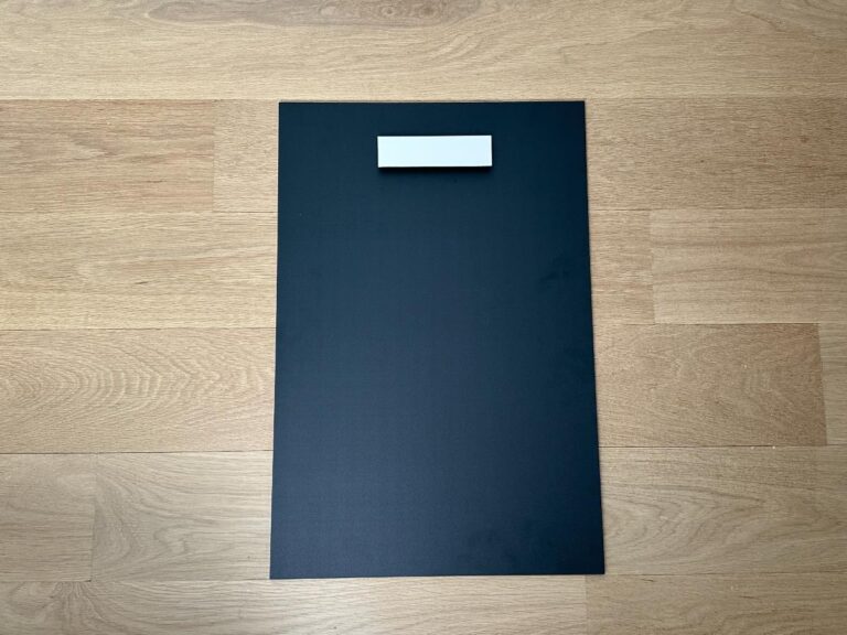 A black rectangular sheet with a white rectangle on top, placed on a light wooden floor.