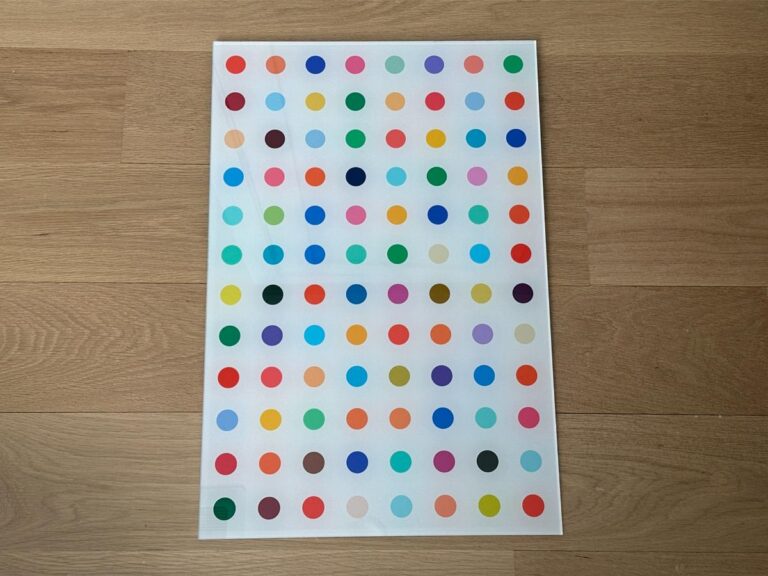 A white sheet with rows of colorful dots is placed on a light wooden floor.