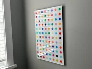 A colorful dot pattern artwork hangs on a gray wall near a window with white blinds.