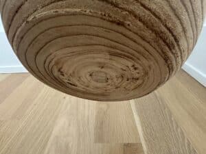 Close-up of a wooden circular object with visible grain patterns, hanging above a light wood floor.