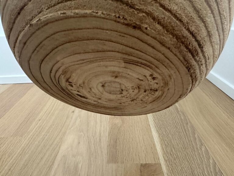 Close-up of a wooden circular object with visible grain patterns, hanging above a light wood floor.