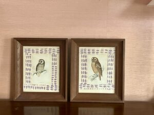 Two framed owl illustrations displayed on a shelf, featuring simple backgrounds with purple patterns.